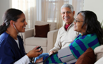 Caregiver helping with blood pressure check for an older woman while her husband sits next to her