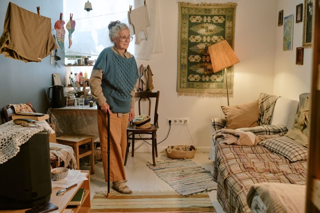 An older woman looks around her cluttered apartment, overwhelmed with household tasks.