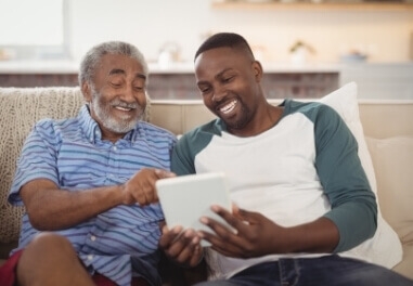 An older man and younger man looking joyfully looking at digital tablet together in Waukesha county.