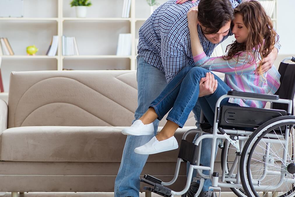Person assisting with placing a woman in her wheelchair.
