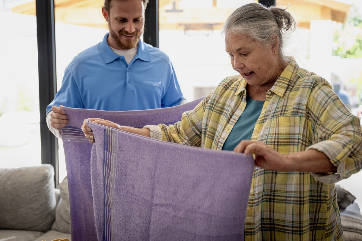 ComForCare Male Caregiver helping a senior woman, both folding laundry together.