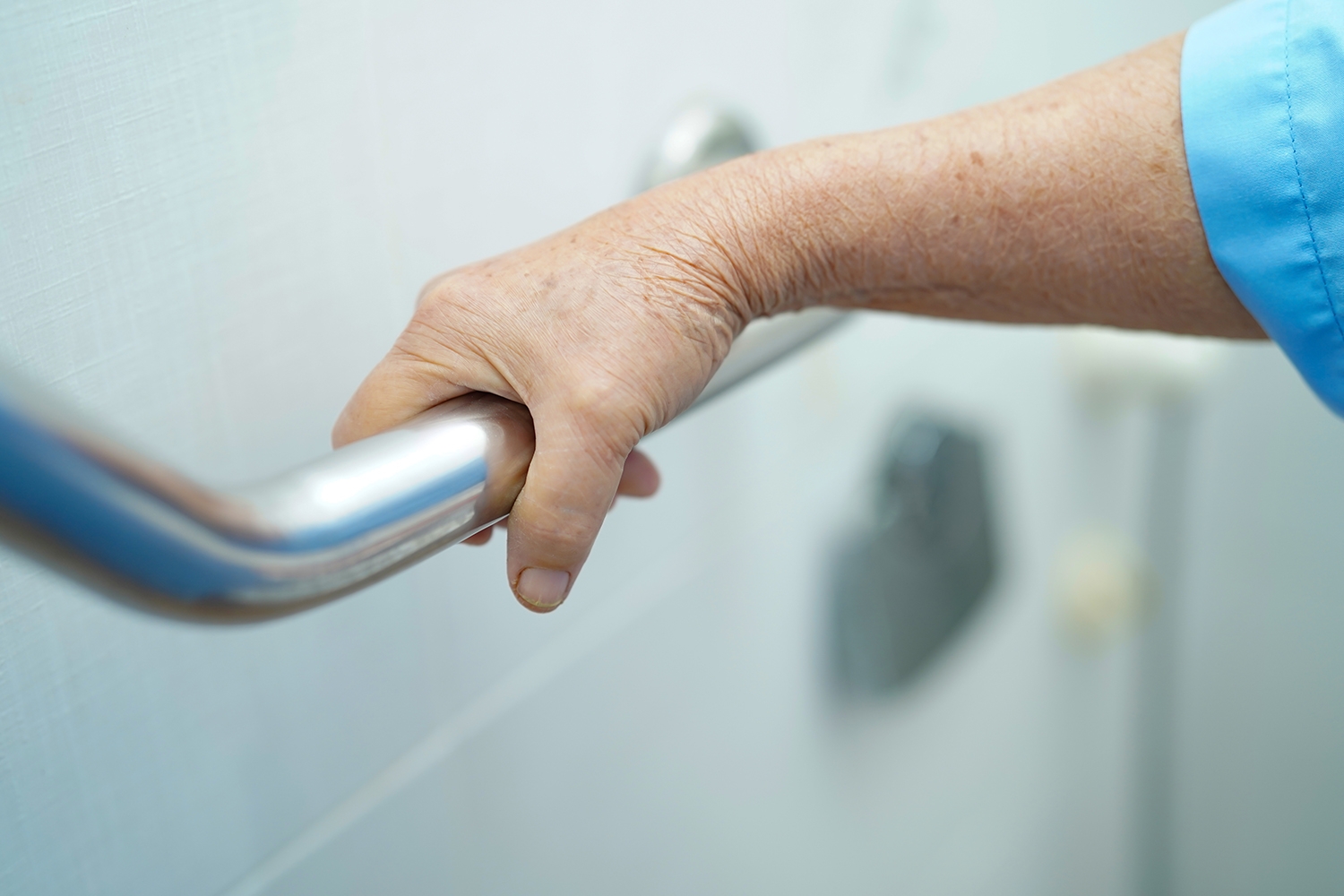 A hand grabbing a grab bar installed in a bathroom.