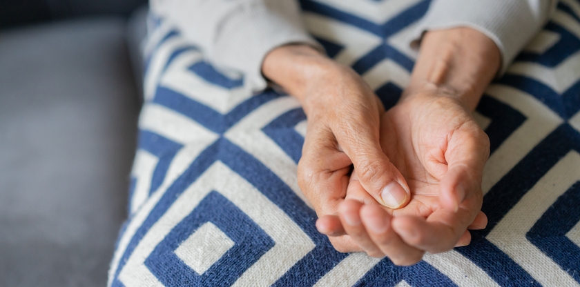 A pair of hands from an older person close up laying in their lap.
