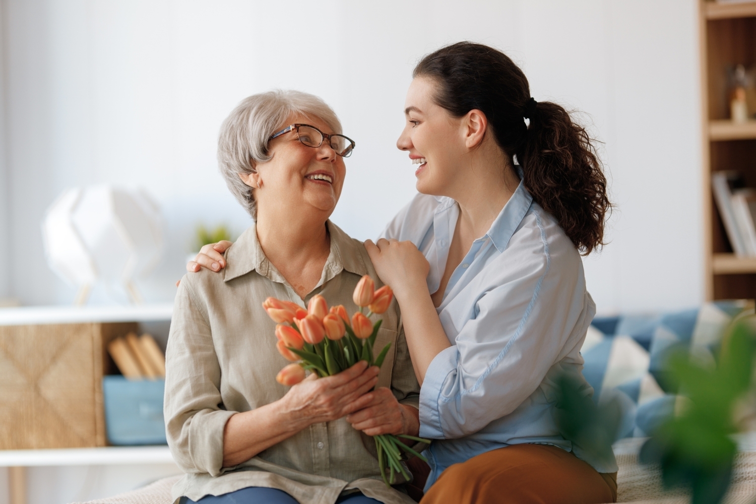 A caregiver comforting an older woman holding a bouquet of Tulips.