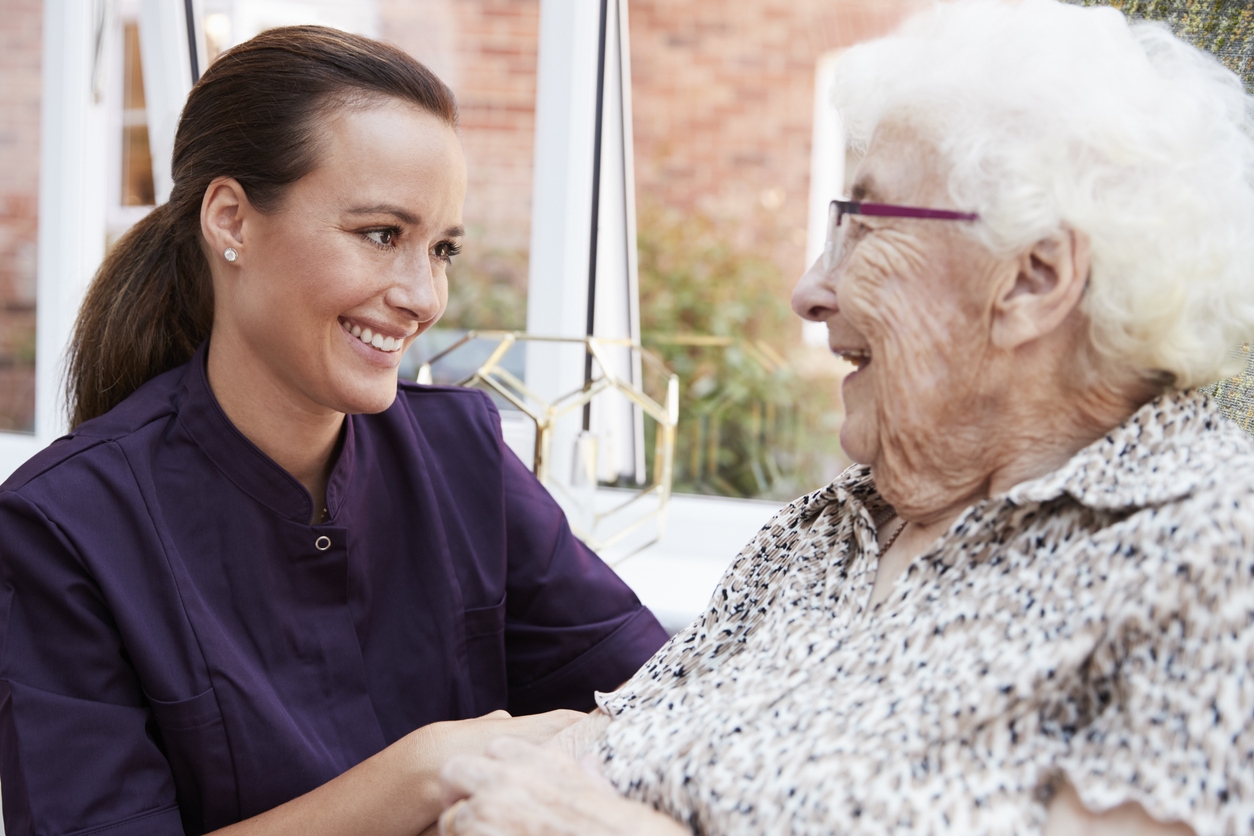 A caregiver talking with an older lady while sitting down.