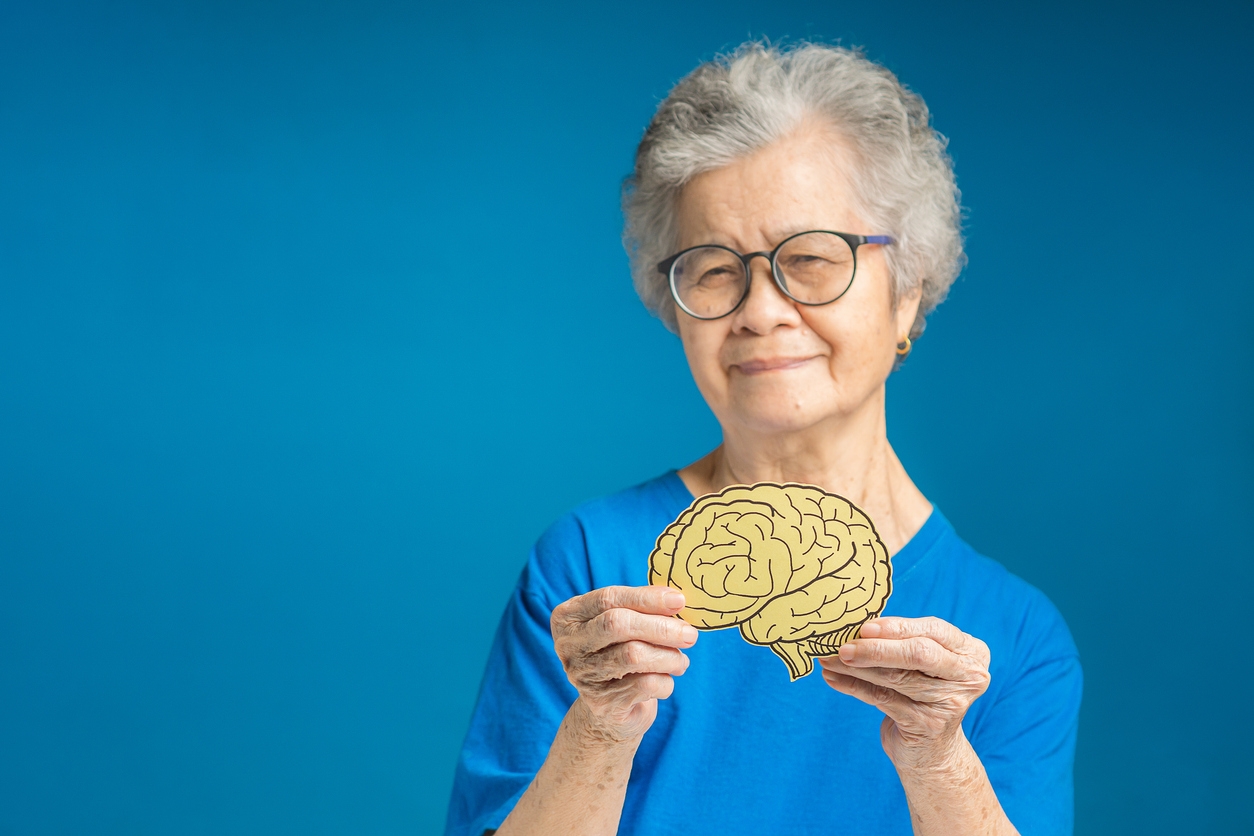 An older lady with glasses holding up an image of a brain.