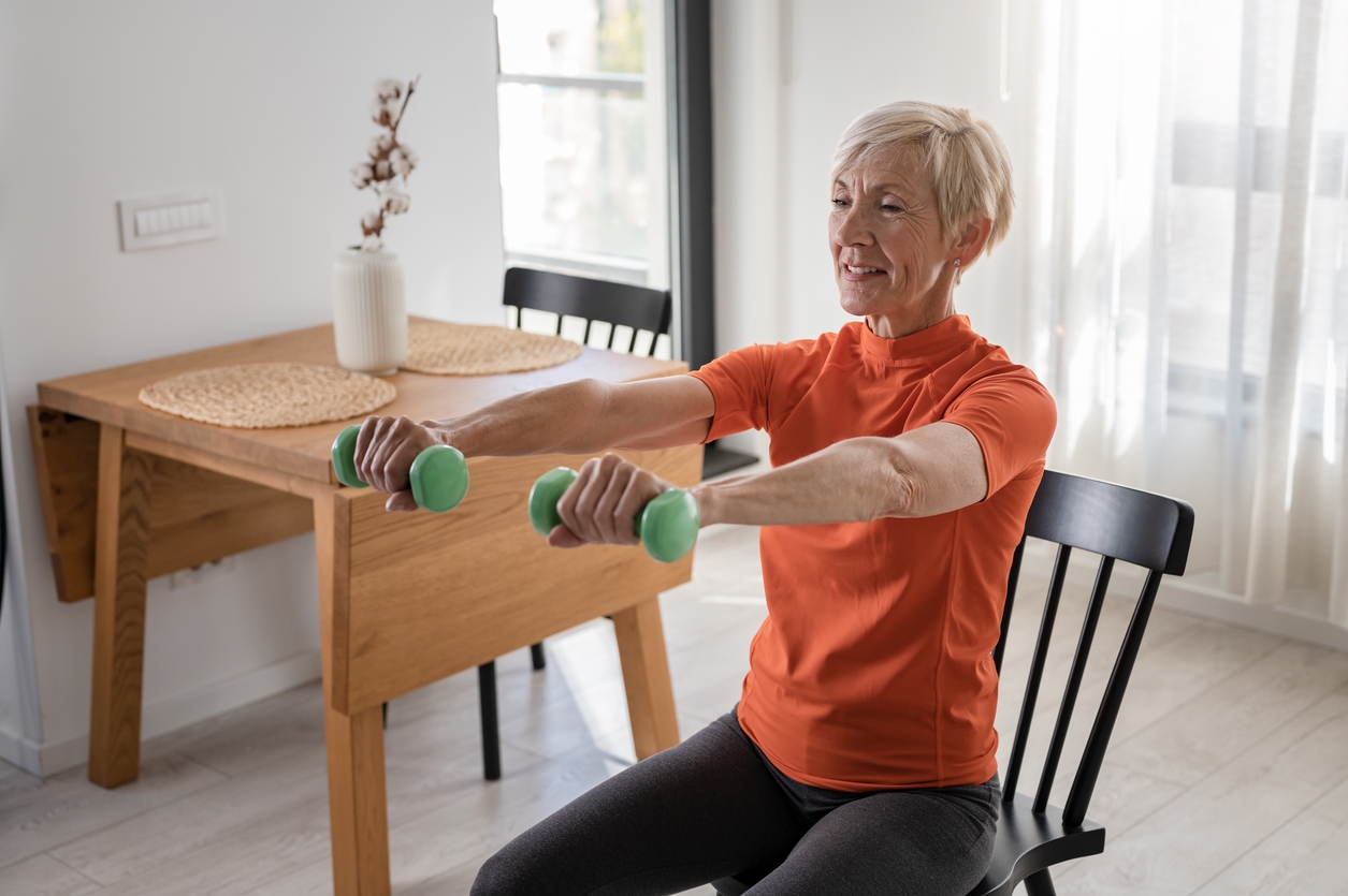 An older woman using hand weights while sitting in a chair.
