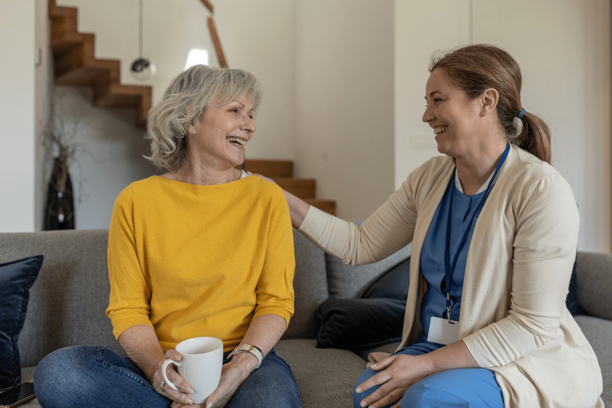 A caregiver sitting and talking with an older lady on a couch.