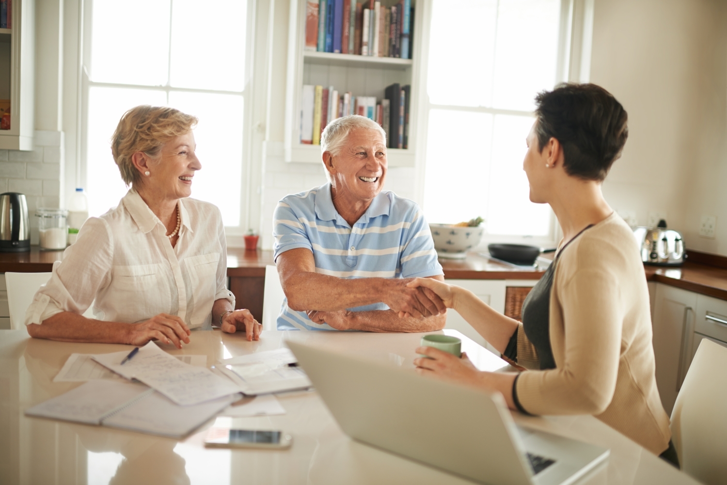 An older couple shaking hand of a care coordinator working on a laptop.
