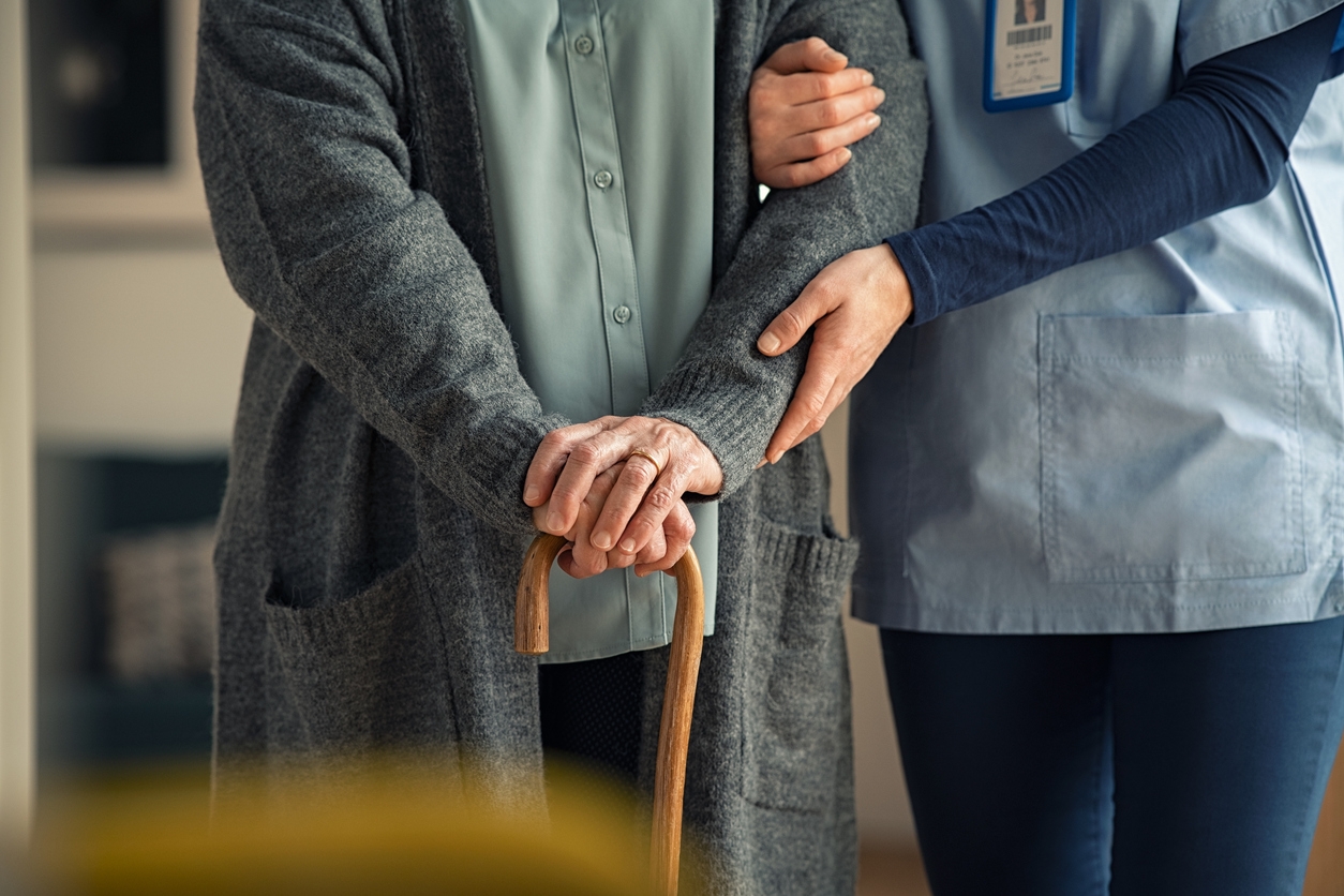 A caregiver supporting an older person using a cane.