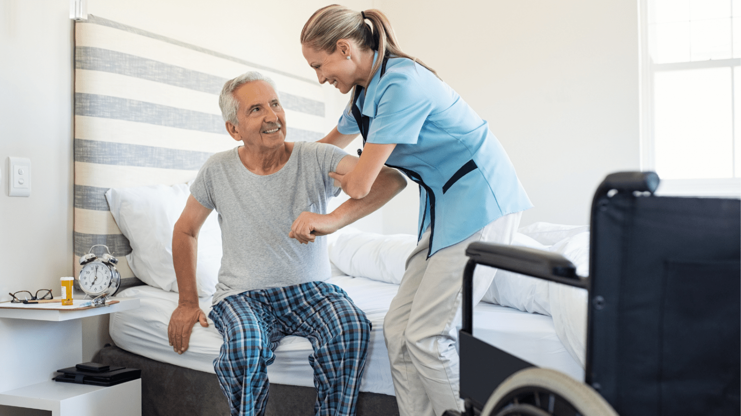 A caregiver helping an older gentleman get out of bed and into a wheelchair.
