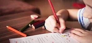 A child writing on a piece of paper with a pencil.