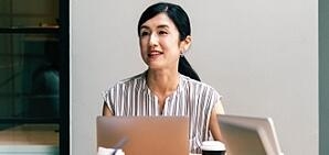 A lady sitting at a conference room table on a laptop.