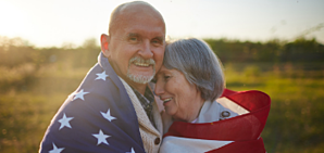An older couple hugging surrounded by an American flag.