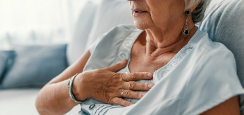An older lady grabbing her chest while sitting down.