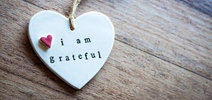 A necklace or small heart piece with the saying "I Am Grateful" on it.
