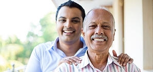 A younger man standing and posing behind an older gentleman for a photo.