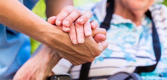 A set of hands from a caregiver and an older person being held in a comforting manner.