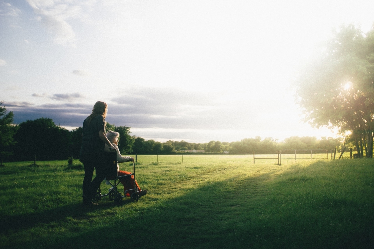 A caregiver pushing an older person in a wheelchair through a field.