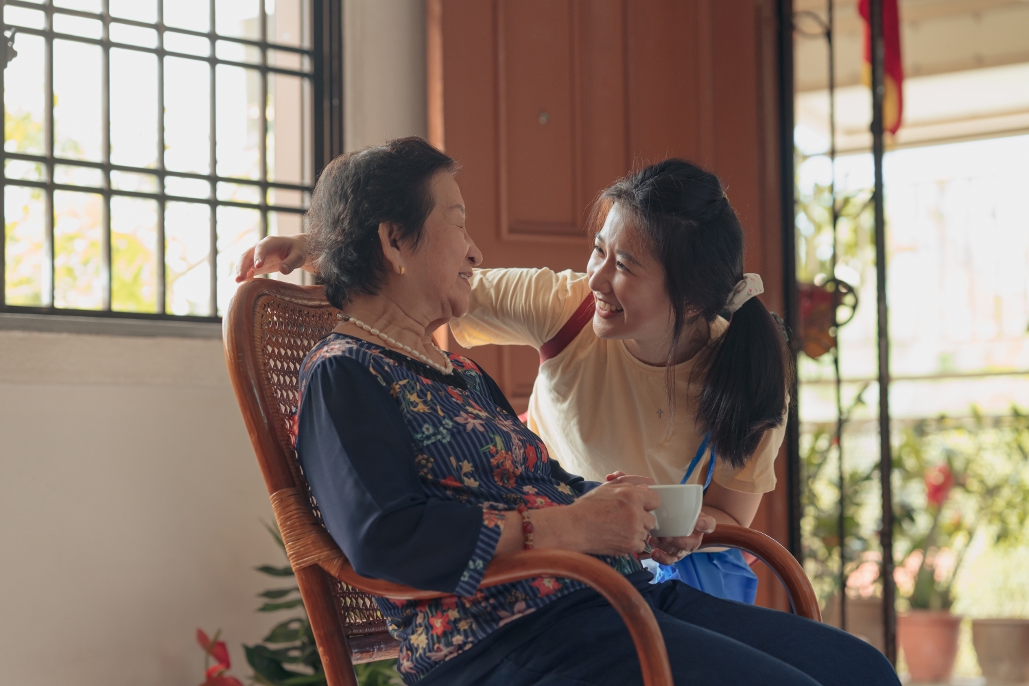 An adult daughter talking with her Mom while she is in a rocking chair.