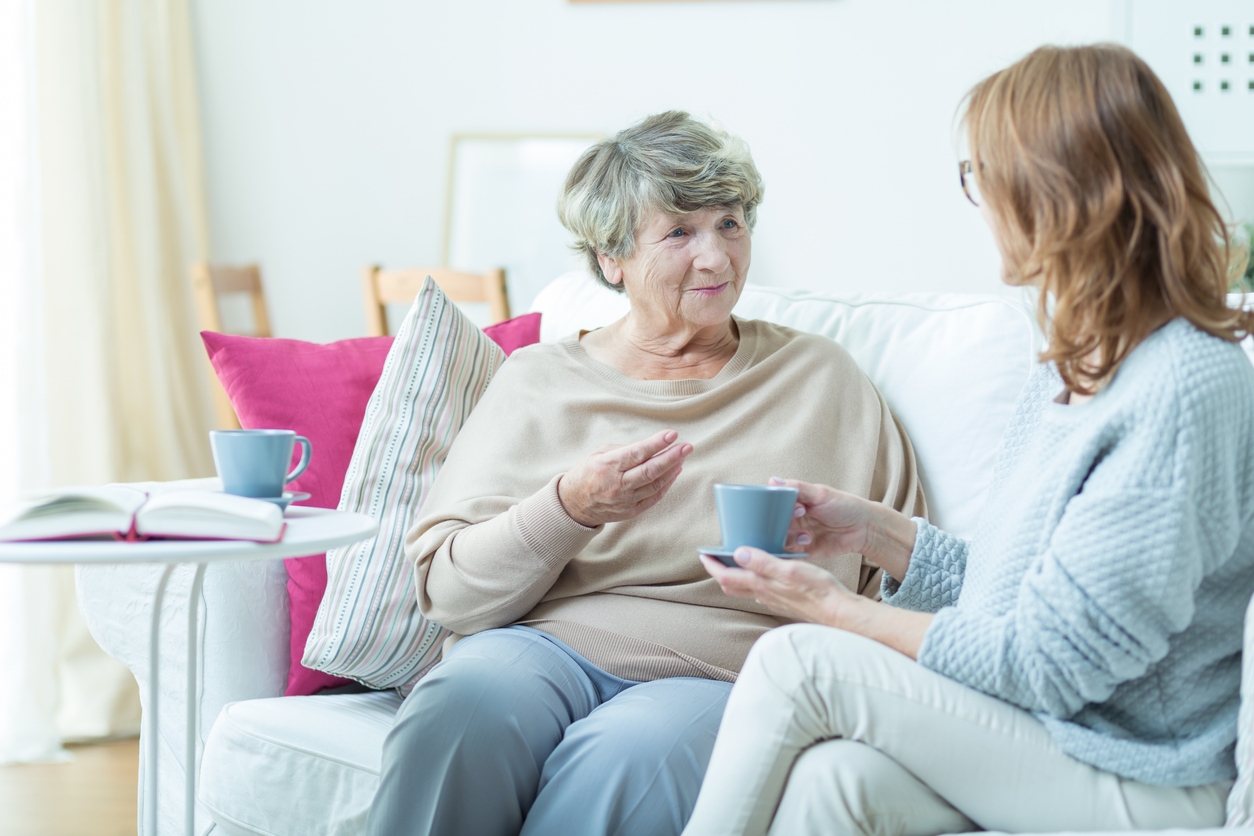 A lady talking with an older woman while enjoying a cup of tea.