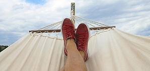 A picture from the point of view of someone laying in a hammock showing their legs and shoes on the other half of the hammock with a cloudy sky in the background.