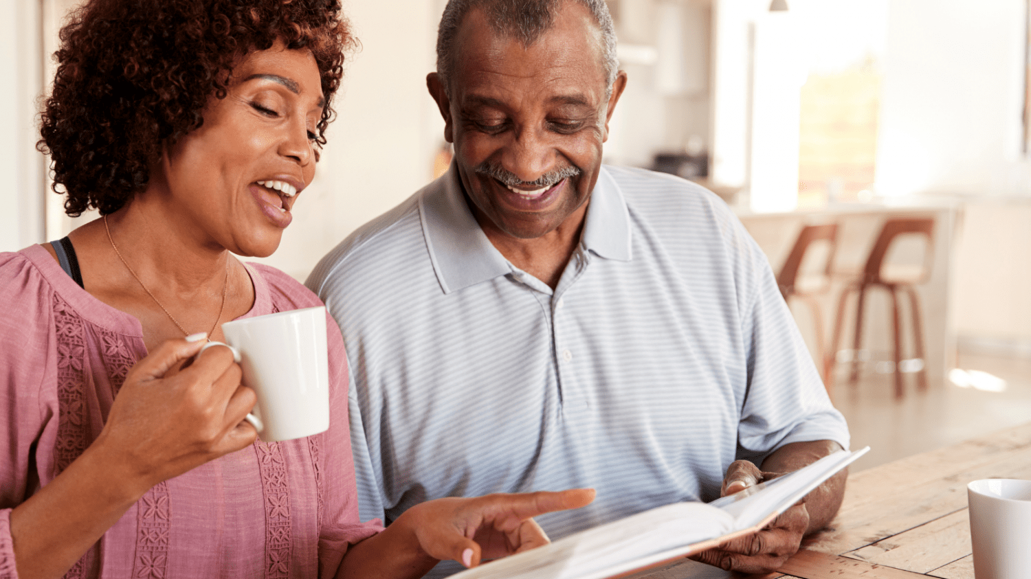 An older couple looking over a photo album together while they drink coffee.